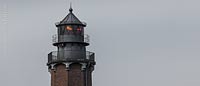  TITEL: »Die Spitze des Leuchtturms Neuland bei Behrensdorf an einem trüben Tag« DETAIL: Im Inneren des Turms zeigt das Foto die noch in Betrieb befindliche Leuchtfeueranlage. Das Gebäude setzt sich markant vom bewölkten Himmel ab. ORT: Ostsee, Hohwachter Bucht, Behrensdorf.