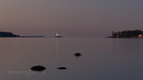 Drei Steine in der ruhigen Heikendorfer Bucht im Abendlicht. Ein Blick über die Heikendorfer Bucht auf den Leuchtturm Friedrichsort und das U-Bootfahrer Ehrenmal an einem windstillen Abend nach Sonnenuntergang.