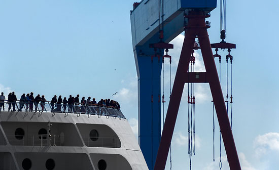 Passagiere einer auslaufenden Fähre vor einem Portalkran im Hafen von Kiel