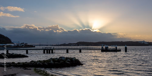  Der Strand und die Seebrücke von Mönkeberg und Sonnenstrahlen am Himmel über Kiel