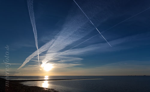 Kondensstreifen am blauen Himmel über dem Wattenmeer bei Norderhafen auf Nordstrand