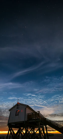 Abendsterne und Wolkenschleier am sommerlichen Himmel über einem Pfahlhaus am Strand von Sankt Peter-Ording