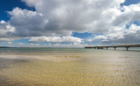 Eine Sandbank im flachen Wasser der Ostsee und die Seebrücke von Scharbeutz an einem sonnige-wolkigen Tag