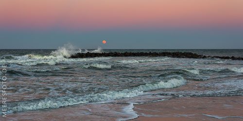 Der rötliche Mond geht hinter den kräftigen Brandungswellen am Schönberger Strand auf