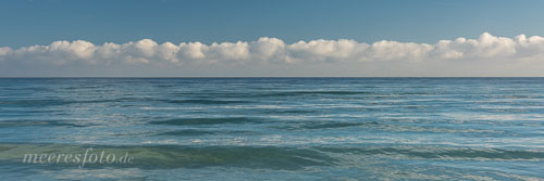 Der blaue Sommerhimmel, eine Wolkenbank und die glänzende Wasseroberfläche der Ostsee vor dem Strand von Sehlendorf
