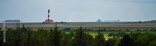 Blick an einem sehr klaren Sommermorgen über Eiderstedt auf den Leuchtturm von Westerhever und die Hafenanlagen von Pellworm am Horizont