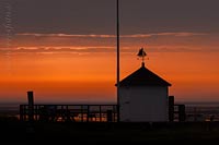  »Kleines Haus im Hafen von Steenode, auf Amrum, vor dem Sonnenaufgang« DETAIL: Der glutrote Horizont kündigt auf diesem Foto, den nahenden Sonnenaufgang an. Ein kleines Haus, markiert den Vordergrund vor dem morgendlichen Watt, welches auf diesem Bild in der fernen Unschärfe liegt.