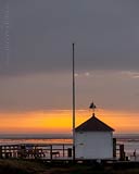  »Kleines Haus im Hafen von Steenode, auf Amrum, bei Sonnenaufgang – 2« DETAIL: Morgendliche Stimmung im Hafen von Steenode. Ein kleines Haus, markiert den Vordergrund vor dem Wattenmeer, welches auf diesem Bild in der fernen Unschärfe liegt.