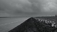  Husumer Hafeneinfahrt und Nordsee-Deich an der Dockkoogspitze unter schweren Morgenwolken – schwarzweiß